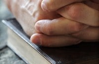 Hands resting on a closed Bible